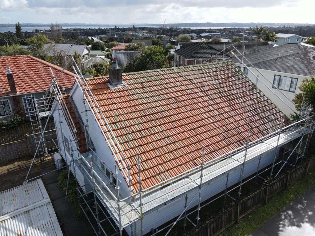 An old terracotta tile roof on a house surrounded by scaffolding.